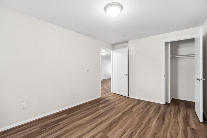 Modern apartment bedroom with elegant wood flooring, ample closet space, and bright ambient lighting.