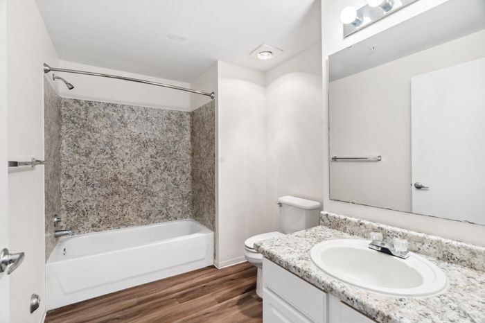 Modern bathroom with a granite sink counter, elegant bathtub, and sleek wooden flooring.
