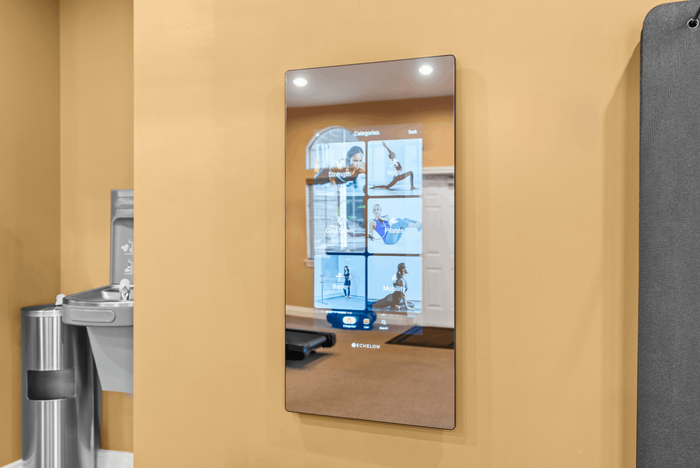 Modern fitness studio with interactive wall-mounted exercise mirror, featuring workout categories like yoga, pilates, and strength training.