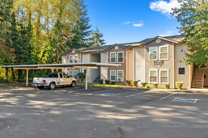 Charming apartment complex with covered parking amid lush green trees, offering serene living in a picturesque setting.
