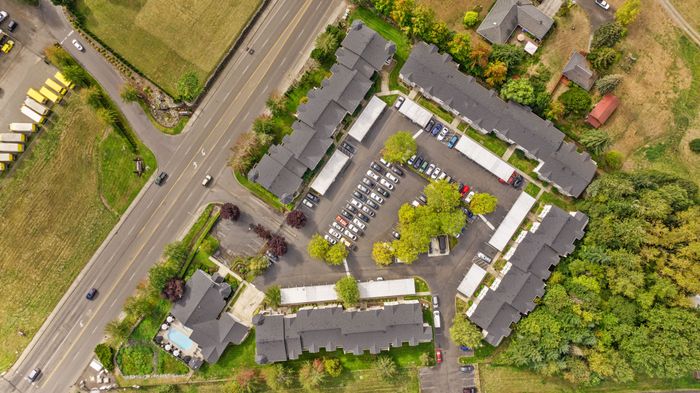 Aerial view of a modern apartment complex with ample parking, lush green surroundings, and nearby roads for easy access.