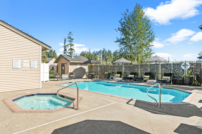 Inviting outdoor pool area with a hot tub, surrounded by cozy loungers and elegant privacy screens, under a vibrant blue sky.