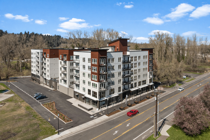 Modern apartment building with multiple balconies, set against a lush natural backdrop, featuring spacious parking and convenient street access.