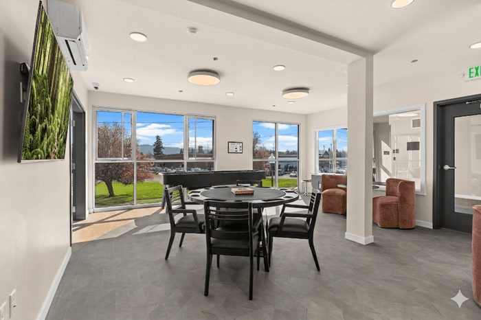 Bright and inviting common area featuring large windows, modern decor, and a versatile round table for social gatherings.