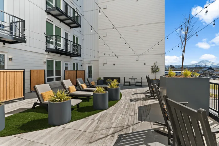 Inviting apartment balcony with modern lounge chairs, vibrant planters, and scenic mountain views under serene blue skies.