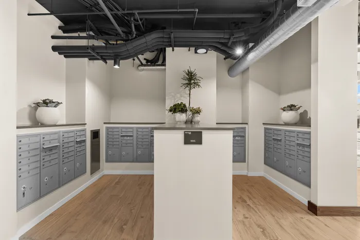 Modern mailroom with elegant wooden flooring, sleek gray mailboxes, and stylish potted plants adding charm to the space.