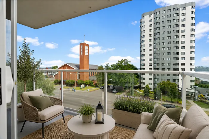 Chic urban balcony overlooking a vibrant cityscape with a modern high-rise and lush greenery, featuring cozy outdoor seating and stylish decor.