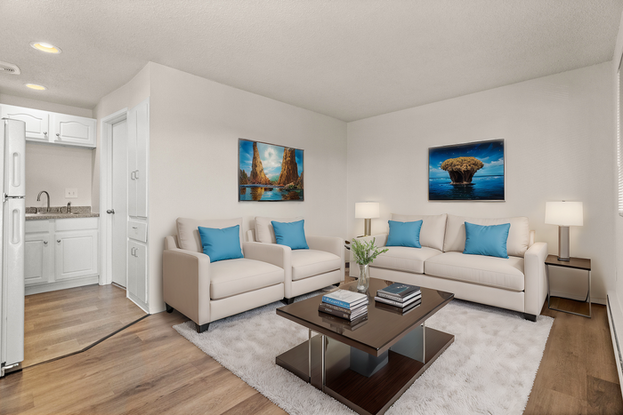 Contemporary living room with plush white sofas, vibrant blue accent pillows, and elegant wooden flooring leading to a cozy kitchenette.