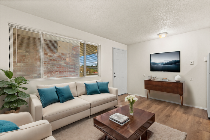 Bright and inviting living room with modern decor, featuring a plush beige sofa and blue accent pillows, complemented by a sleek wooden coffee table with fresh flowers.
