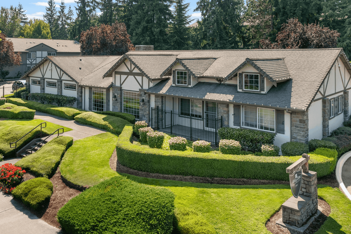 Charming Tudor-style home with beautifully manicured gardens and lush green lawns, set against a backdrop of mature trees.