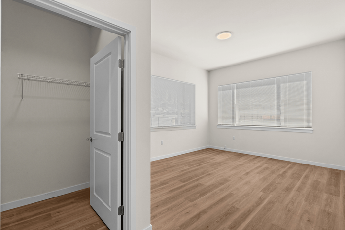 Bright and spacious bedroom with large windows, sleek wooden floors, and a built-in closet for ample storage.