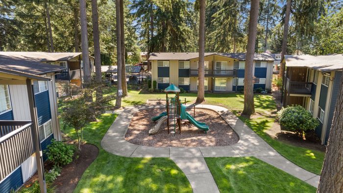 Charming apartment community featuring lush greenery, tall trees, and a well-maintained playground, ideal for family living.