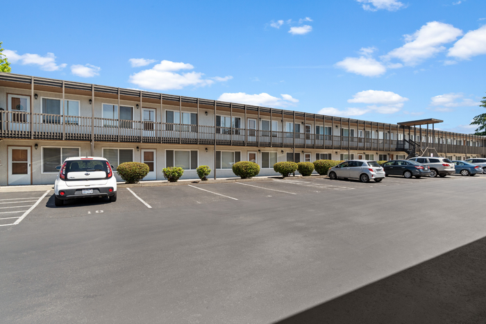 Charming two-story apartment complex with ample parking and manicured landscaping under a clear blue sky.