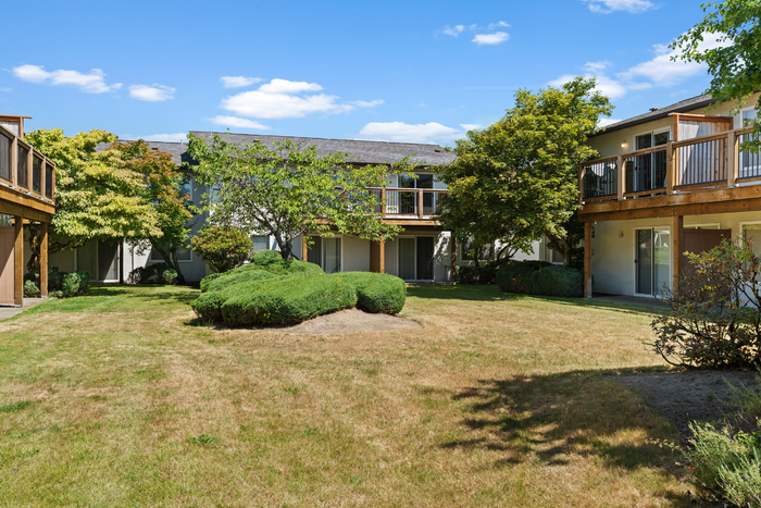 Charming apartment complex courtyard with lush greenery, wooden balconies, and serene open-air spaces under a bright blue sky.