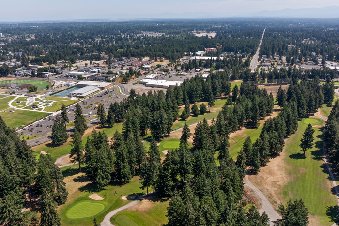 Breathtaking aerial view showcasing lush, green landscape with a golf course surrounded by dense forest, intersected by a scenic pathway and neighboring a well-structured community.