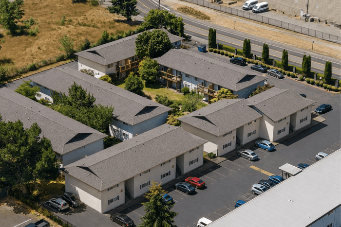 Aerial view of a serene apartment complex with multiple buildings surrounded by lush greenery and ample parking space.