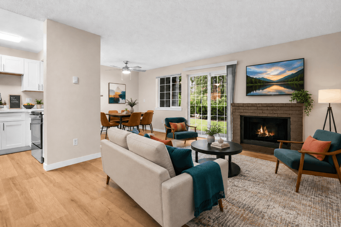 Charming open-concept living area showcasing a cozy fireplace, elegant dining space, and modern kitchen, bathed in natural light with lush garden views.