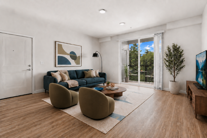 Bright and inviting living room with a plush navy sofa, modern artwork, and floor-to-ceiling windows opening to lush greenery.