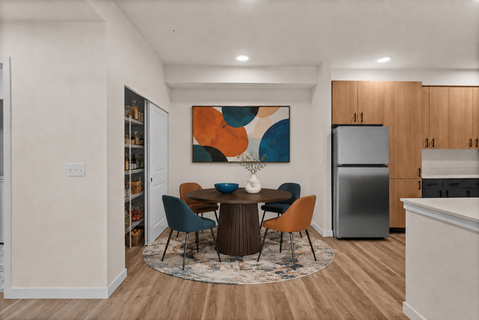 Modern kitchen and dining area with elegant wood flooring, vibrant abstract art, and chic seating around a round table. Sleek cabinetry and stainless steel appliances enhance the stylish space.