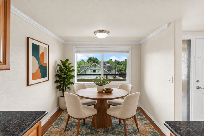 Bright dining area with elegant round table, four cozy chairs, and a view of lush greenery through a large window, enhanced by modern art and natural decor.
