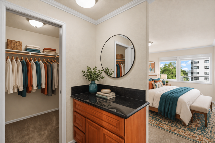 Elegant bedroom with a cozy walk-in closet, featuring a neatly organized wardrobe and a stylish vanity area with a circular mirror, perfect for modern living.