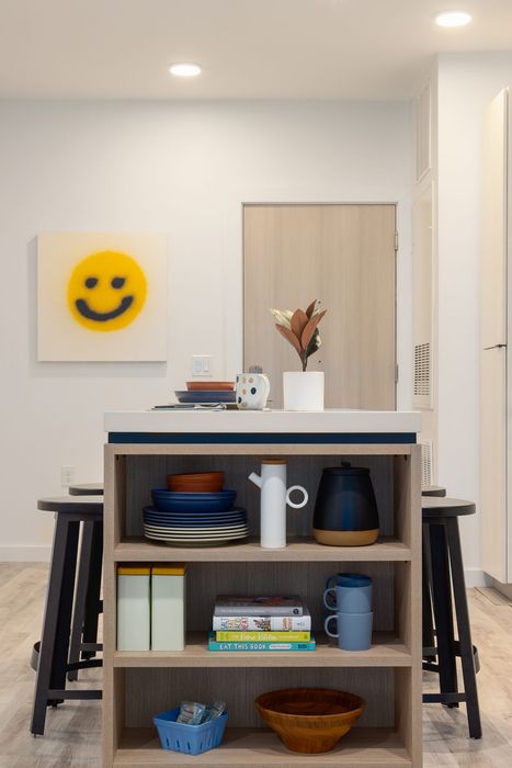 Contemporary kitchen nook with modern decor, featuring a cheerful smiley face artwork, open shelving with stylish crockery, and inviting wood accents.