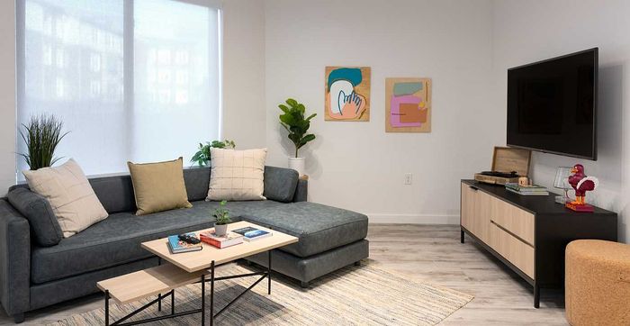 Inviting living room with a sleek grey sectional, modern art pieces, and a large flat-screen TV creating a cozy entertainment space.