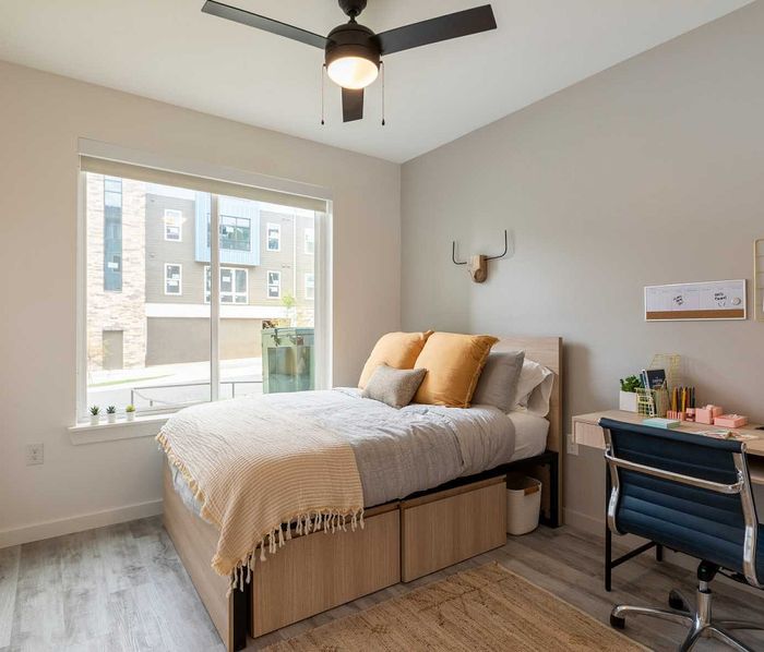 Bright and modern bedroom featuring large window, cozy bed with soft pillows, chic desk, and stylish decor.