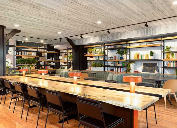 Trendy and inviting co-working space with modern wooden tables, ambient lighting, and lush greenery throughout the stylish interior.