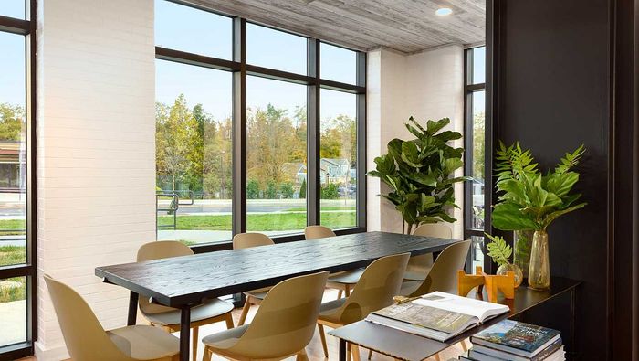 Bright and modern dining area with large windows, sleek furniture, and lush greenery, offering a warm, inviting atmosphere.