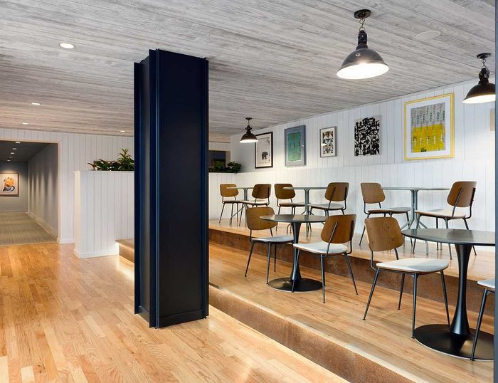 Chic communal area with stylish wooden chairs, modern artwork, and ambient lighting, perfect for meeting or relaxation.