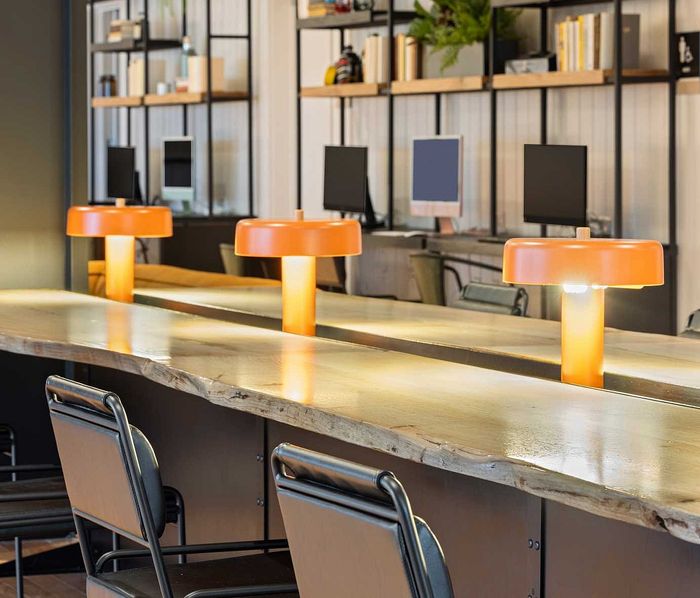 Modern coworking space with sleek wooden desks, vibrant orange lamps, and stylish shelving.