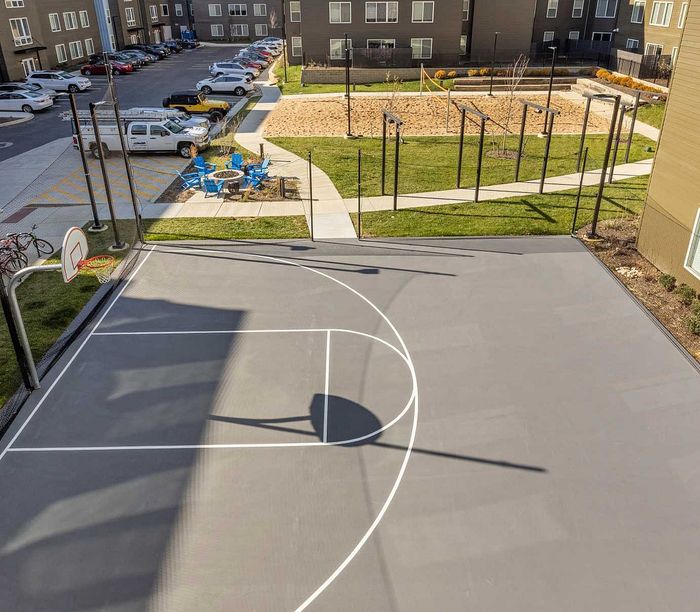 Modern apartment complex featuring a recreational basketball court, landscaped grounds, and cozy outdoor seating area under sunny skies.