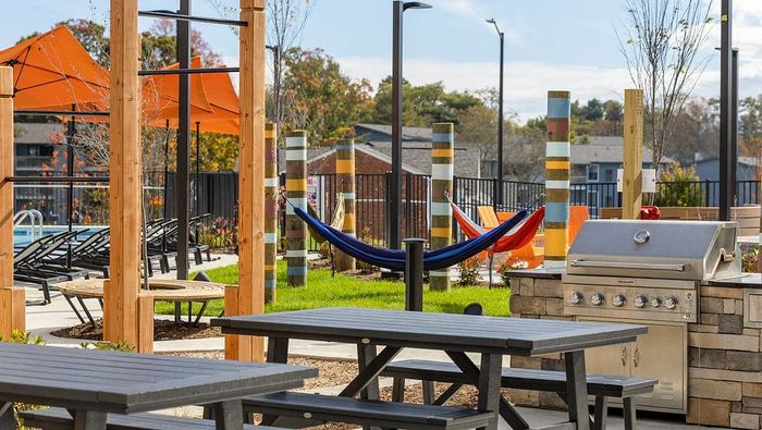 Vibrant outdoor apartment amenities featuring picnic tables, a barbecue grill, and colorful hammocks under orange sun shades, providing a perfect mix of relaxation and entertainment.
