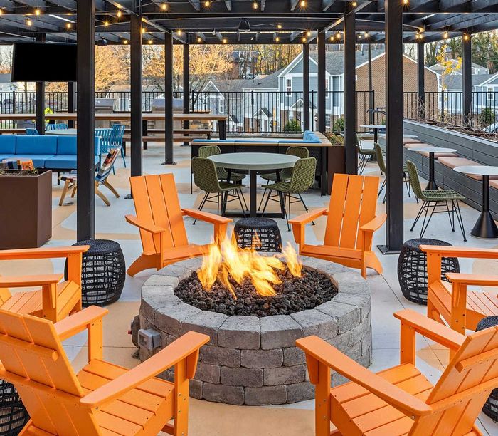 Inviting outdoor patio with vibrant orange chairs around a cozy fire pit, surrounded by modern furniture and twinkling string lights.