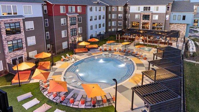 Luxurious apartment complex featuring a resort-style pool, ample lounge chairs, vibrant orange umbrellas, and modern architecture.