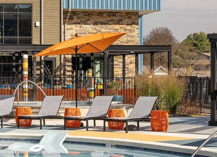 Chic outdoor patio featuring poolside lounge chairs, vibrant orange umbrellas, and modern architecture.