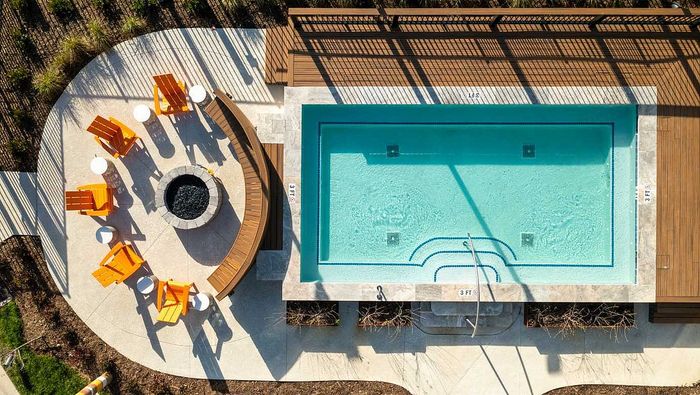 Luxurious aerial view of a serene poolside area featuring vibrant orange lounge chairs and a circular fire pit, perfect for relaxation and entertainment.