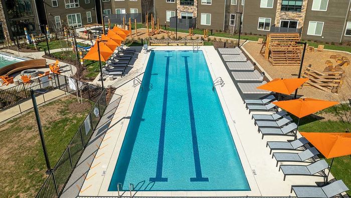 Luxurious outdoor pool area featuring sleek loungers and vibrant orange umbrellas, surrounded by modern apartment buildings and landscaped greenery.