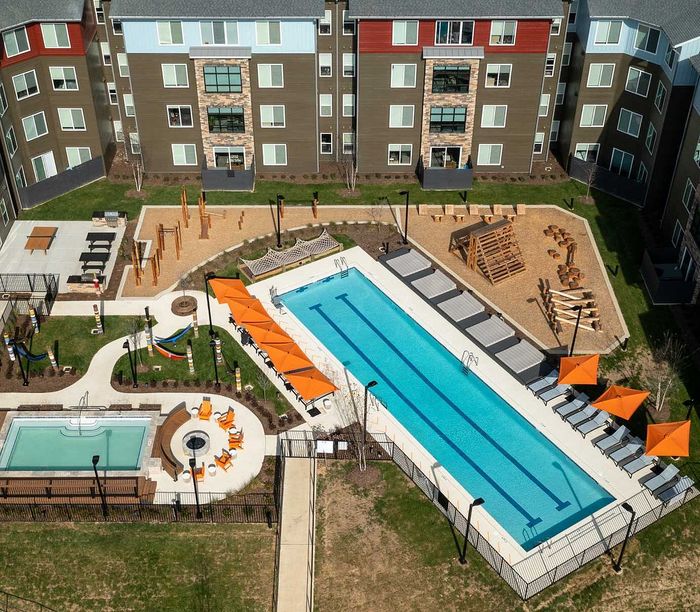 Vibrant apartment complex with a large swimming pool, orange parasols, inviting lounge area, playground, and modern building facade.