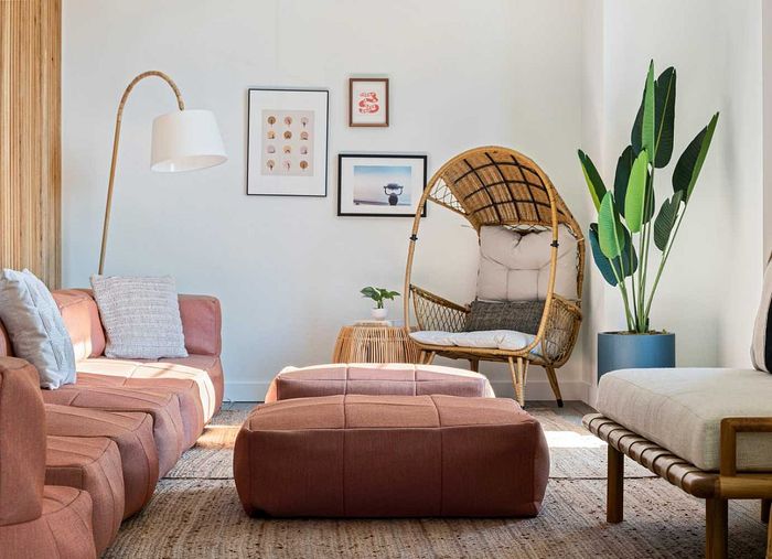 Inviting living room with cozy pink sectional sofa, stylish wicker chair, modern floor lamp, vibrant artwork, and lush indoor plant.