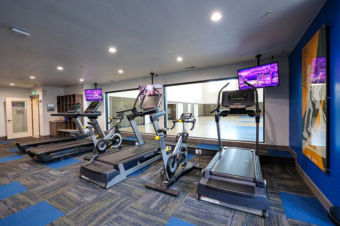 Modern fitness center with treadmills and exercise bike, featuring vibrant lighting and wall displays.