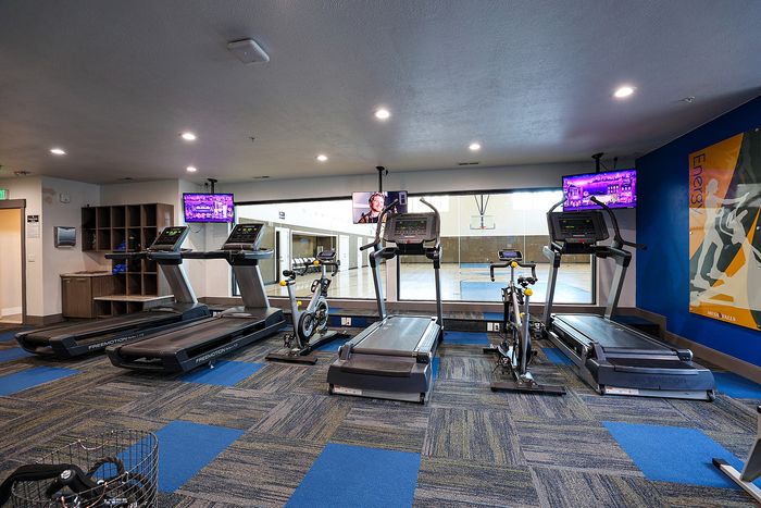 Modern fitness center with treadmills and stationary bikes overlooking a basketball court.