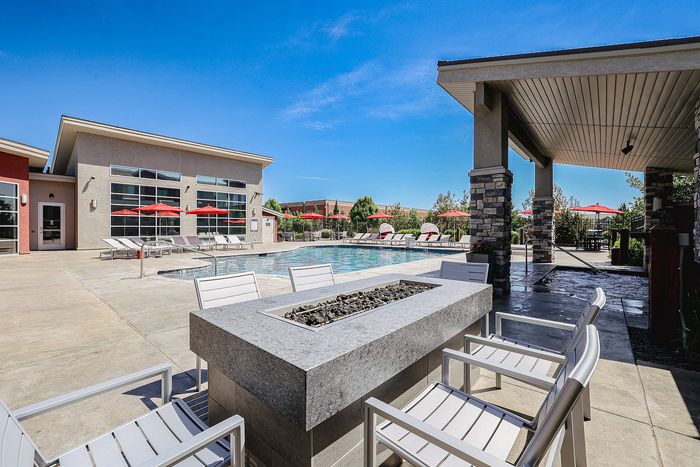 Luxurious outdoor pool area with modern fire pit, stylish lounge chairs, and vibrant red umbrellas under a clear blue sky.