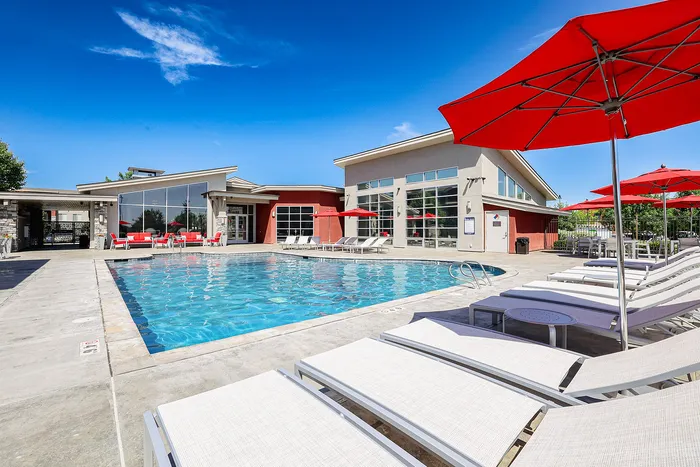 Luxurious outdoor pool area with sleek lounge chairs and vibrant red umbrellas, perfect for relaxing under a clear blue sky.