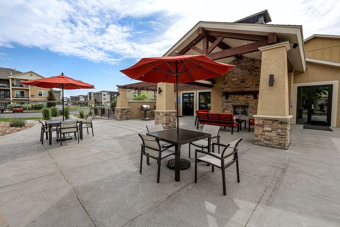 Charming outdoor patio space featuring stylish red umbrellas, contemporary seating, and a cozy fireplace in a serene apartment complex setting.