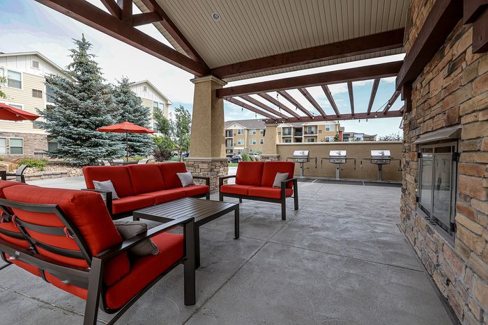 Inviting outdoor patio with red cushioned seating, modern grill stations, and charming wooden pergola, perfect for entertaining.