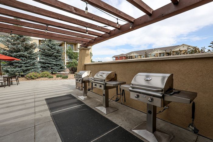 Inviting outdoor patio with modern stainless steel grills under a charming wooden pergola, surrounded by lush greenery and scenic views.