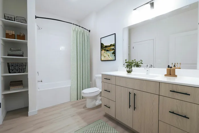 Modern bathroom with elegant vanity, stylish open shelving, and inviting tub featuring a chic green curtain.