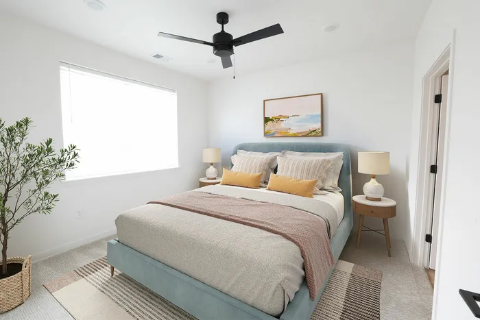 Bright and airy bedroom with a plush, light blue bed, stylish decor, and abundant natural light from a large window.
